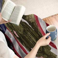 Person indoors holding hot beverage with tactical military flag blanket.