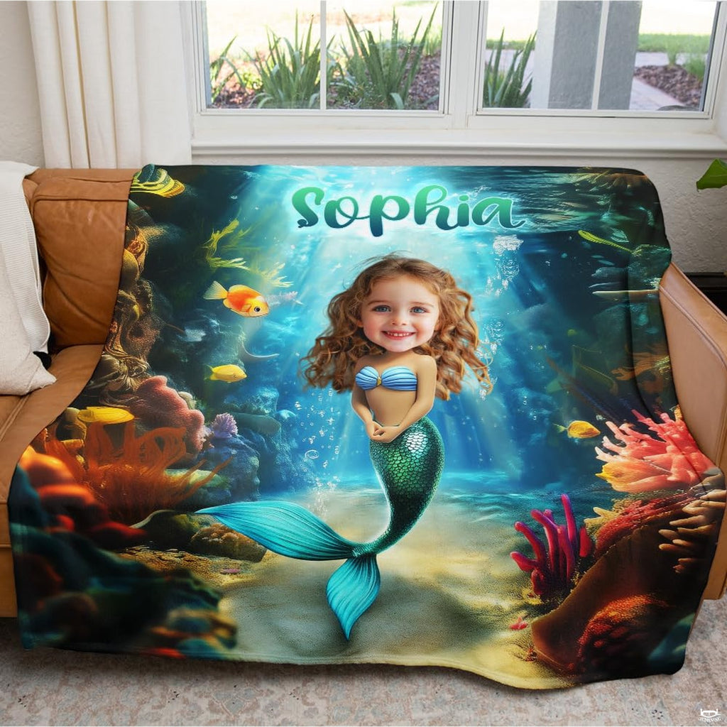 Mermaid graphic throw blanket neatly draped across brown leather living room sofa by a sunny window.