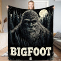 Sasquatch face illustration against a full moon, stars, and evergreen pines on a decorative throw blanket