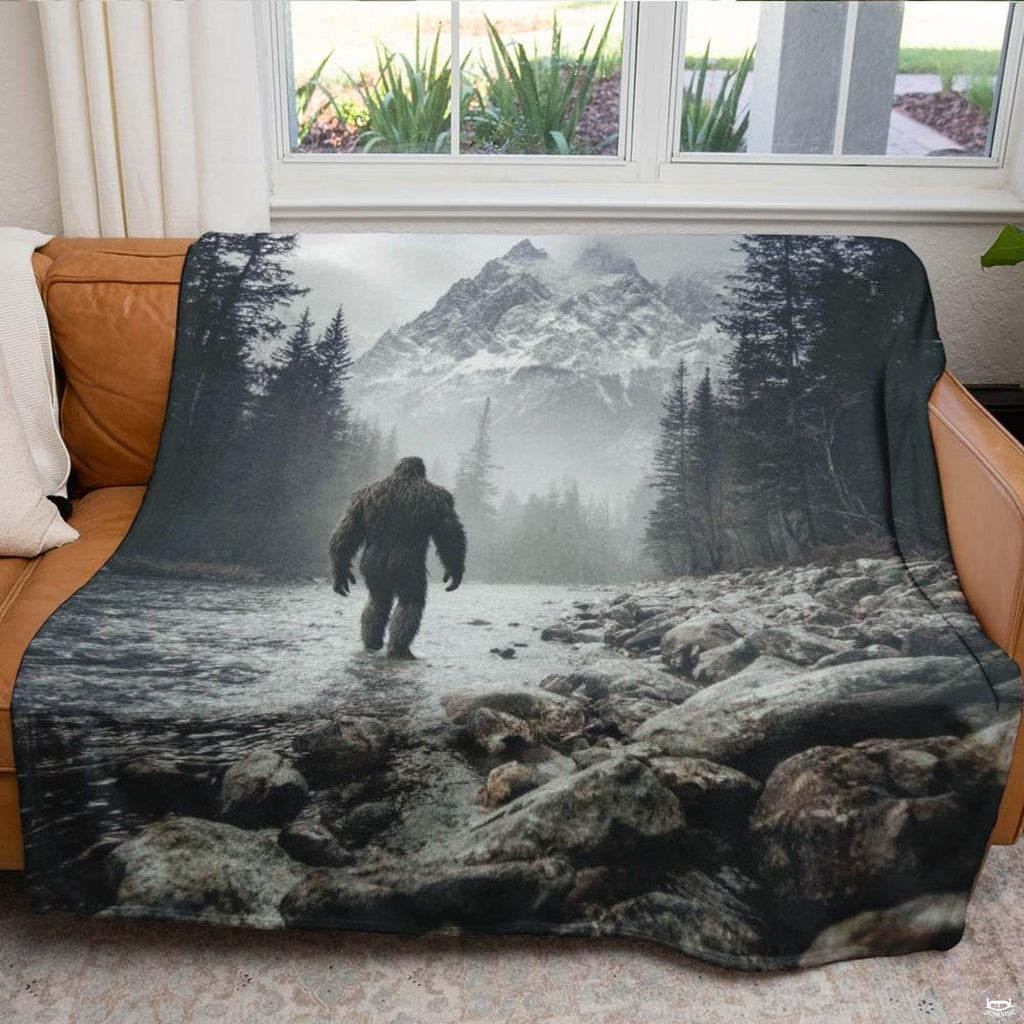 Bigfoot walking through a rocky mountain river toward snow-capped peaks, view 5.