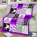 Purple wrestling patchwork blanket draped over a living room couch beside a stack of books.