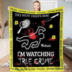Woman holding up black crime scene blanket featuring chalk outline and yellow police tape