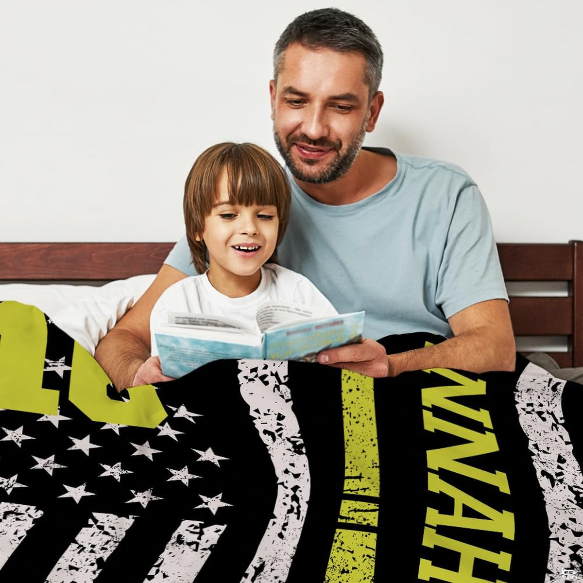 Parent and child reading a book in bed draped in the distressed softball flag print.