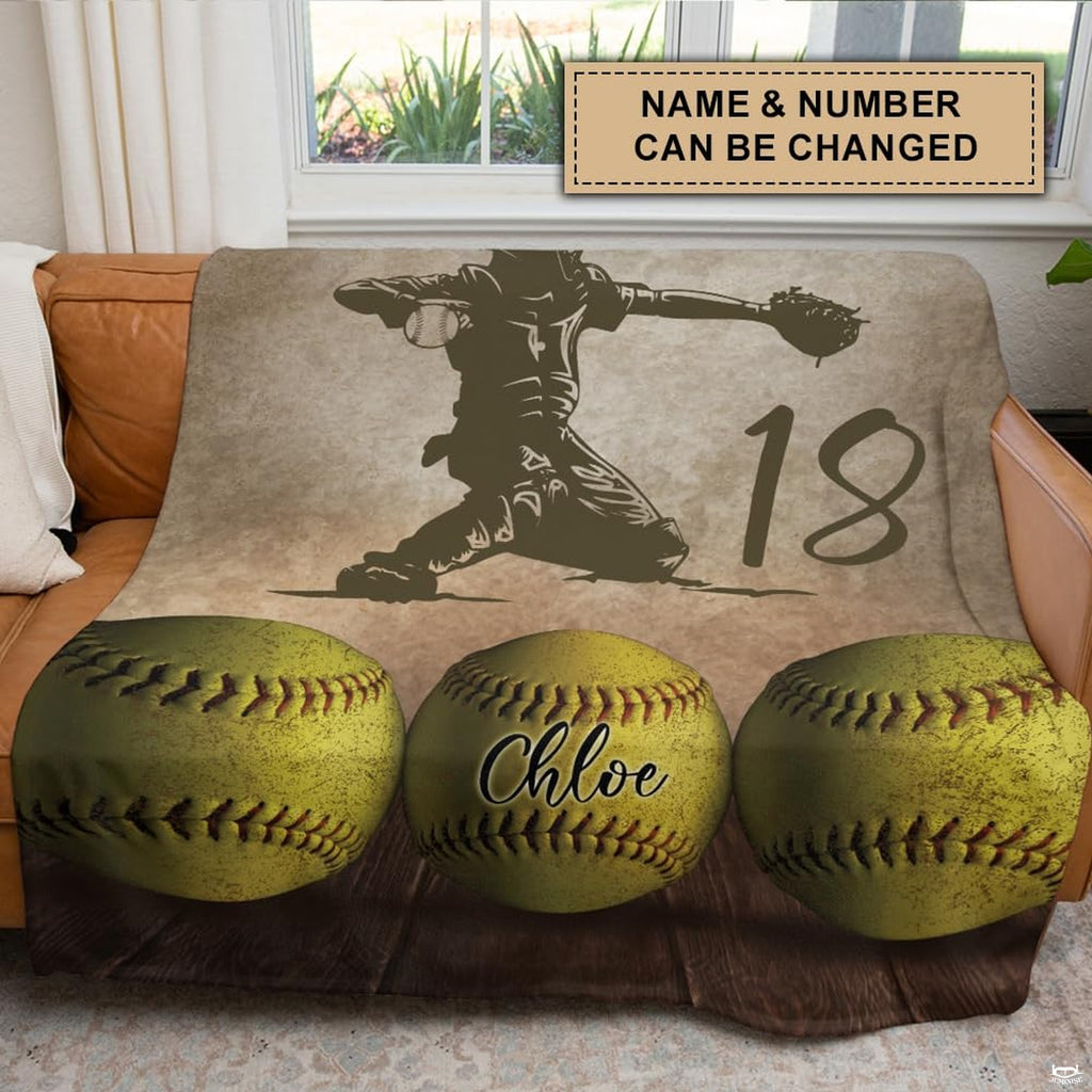 Softball catcher graphic throw blanket draped across a brown leather couch in a modern space.