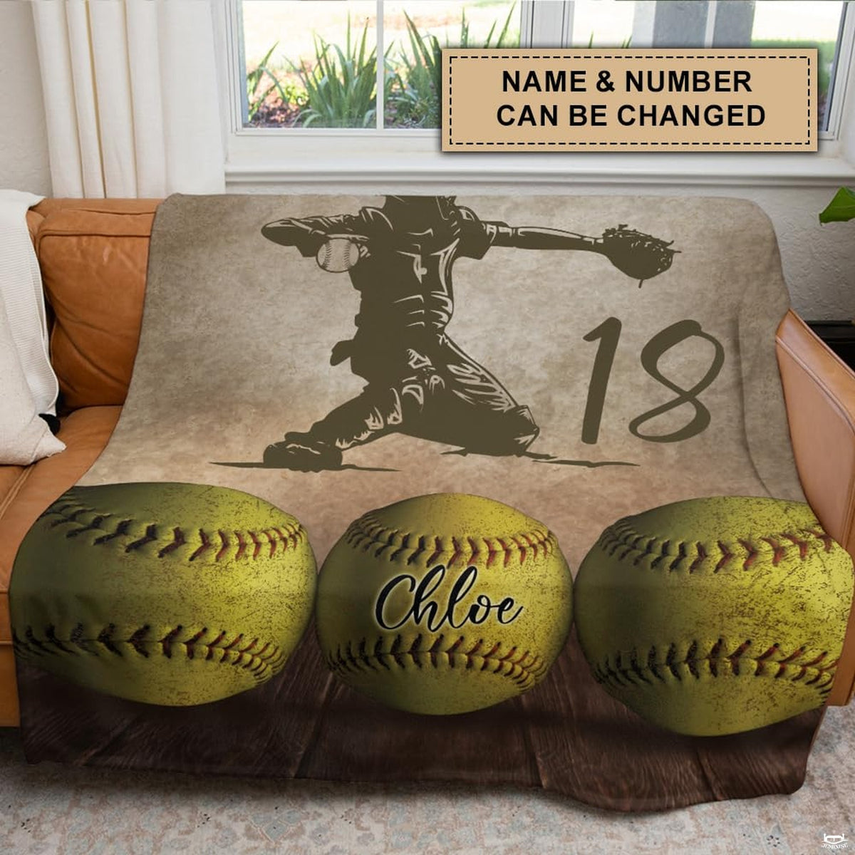 Softball catcher graphic throw blanket draped across a brown leather couch in a modern space.