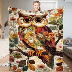 Whimsical collage-style horned owl perched on a branch amid autumn leaves on a throw blanket