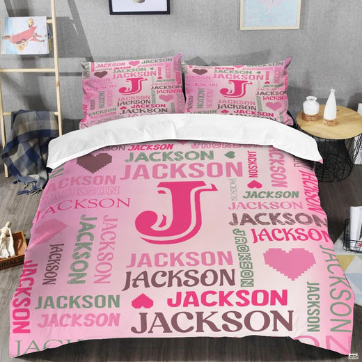 Pink monogram bedding displaying bold magenta initial letter surrounded by multidirectional word-cloud typography