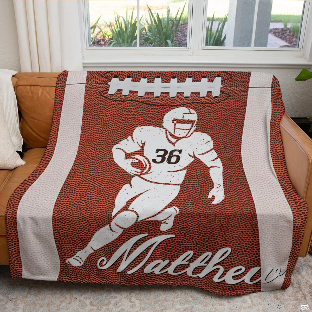 Football runner graphic throw blanket draped neatly across a brown leather couch in a modern room.