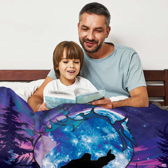 Father and son reading storybook together in bed under glowing blue moon Bigfoot graphic throw blanket.