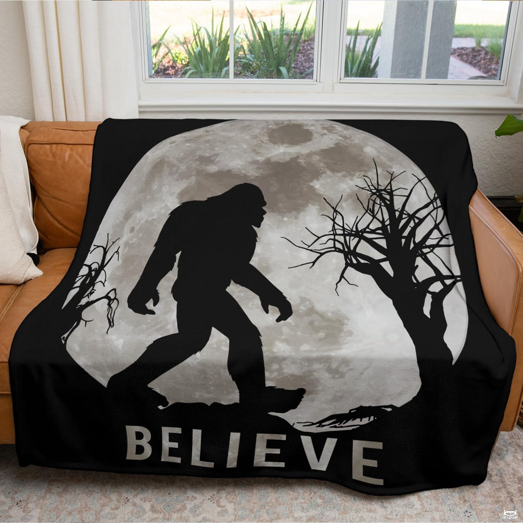 Full moon Sasquatch blanket neatly draped across a living room couch in front of a window.