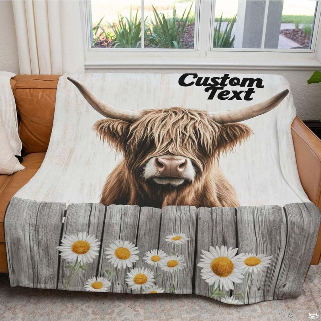 Folded rustic daisy fence Highland cow throw blanket resting on wooden table displaying rustic print