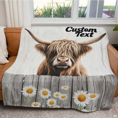 Folded rustic daisy fence Highland cow throw blanket resting on wooden table displaying rustic print