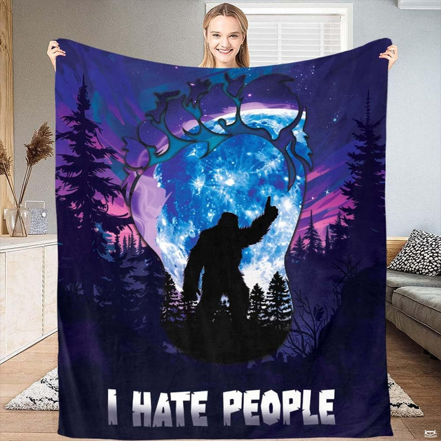 Woman displaying dark indigo Bigfoot footprint throw blanket with glowing blue moon and pine forest.