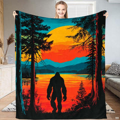 Person holding a Bigfoot lakeside sunset throw blanket displaying cryptid silhouette and glowing orange sun