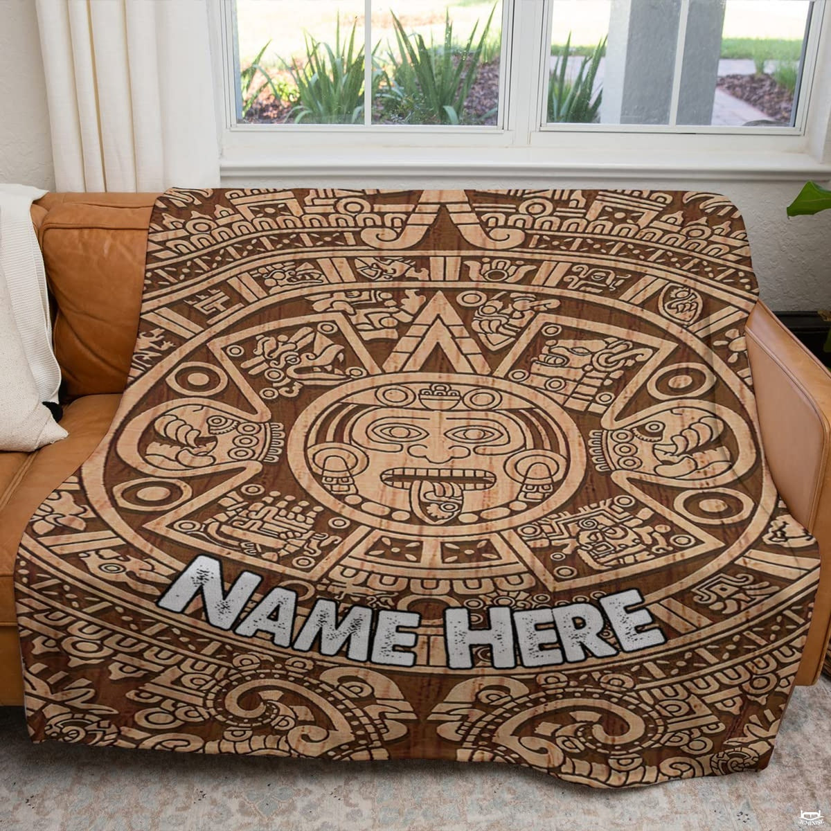 Carved timber sun stone calendar textile displayed across a brown couch in sunlit room.