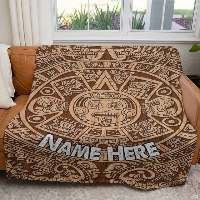 Carved timber sun stone calendar textile displayed across a brown couch in sunlit room.