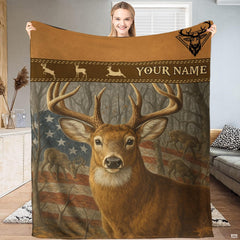 Model holding up an outdoor blanket displaying a whitetail buck before an American flag and woodland trees.