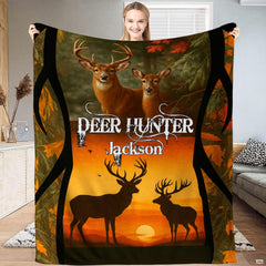 Model holding up a wildlife blanket displaying whitetail bucks and silhouetted stags before an amber sunset.