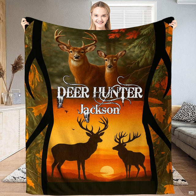 Model holding up a wildlife blanket displaying whitetail bucks and silhouetted stags before an amber sunset.