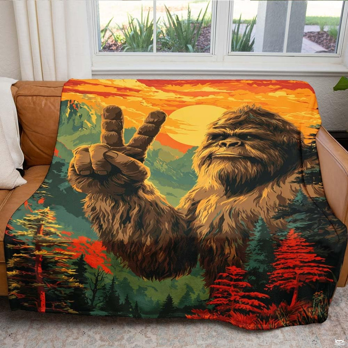 Colorful sunset Bigfoot blanket draped over an indoor living room couch near a bright window.