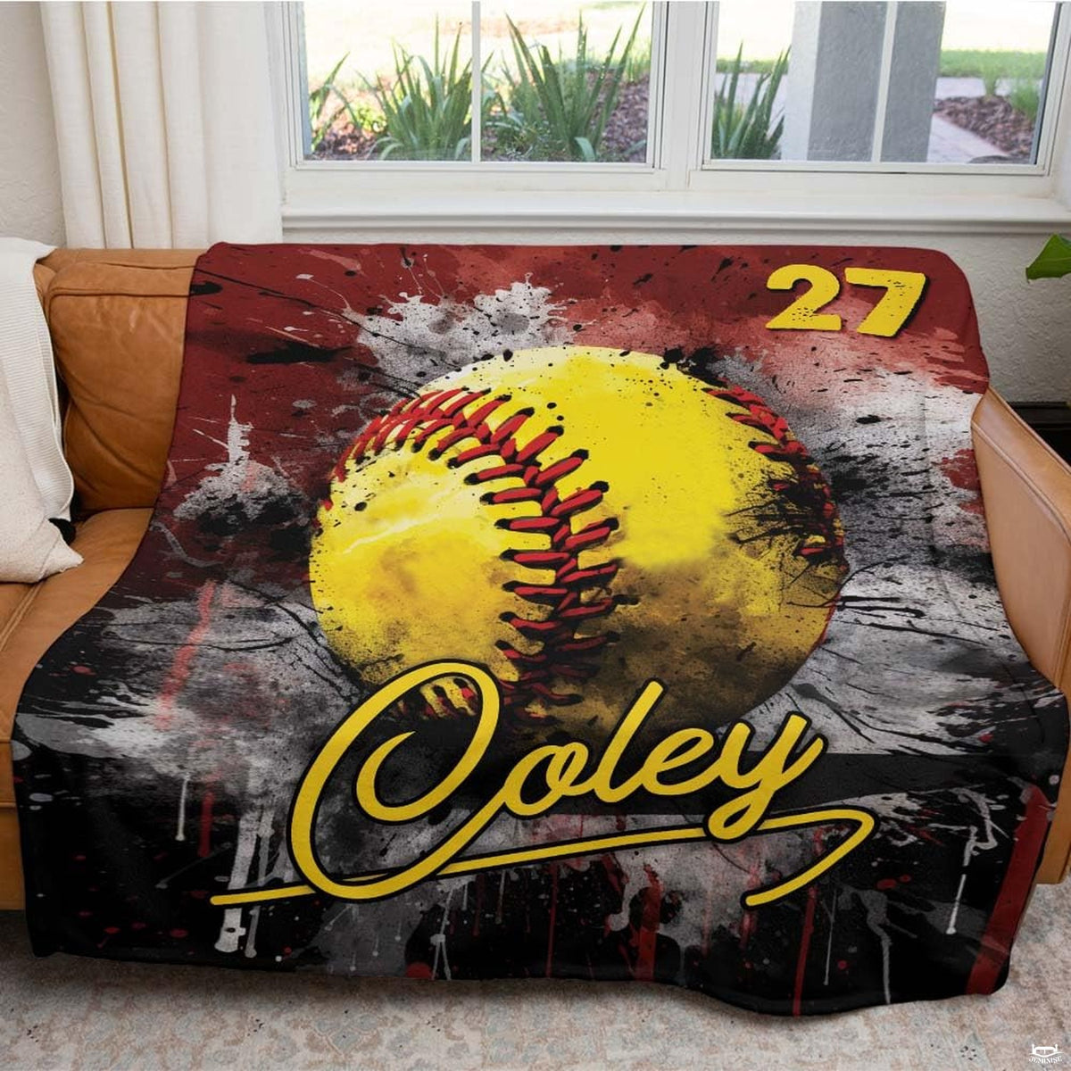 Softball throw blanket arranged neatly across brown leather living room sofa