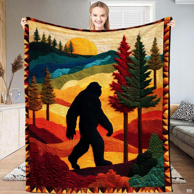 Person displaying a folk art Bigfoot throw blanket featuring autumn hills, pine trees, and a golden sun