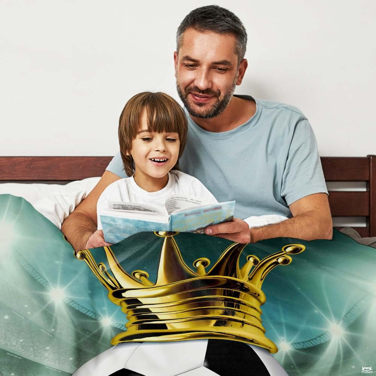 Father and child relaxing together indoors reading a book with crowned soccer design blanket.