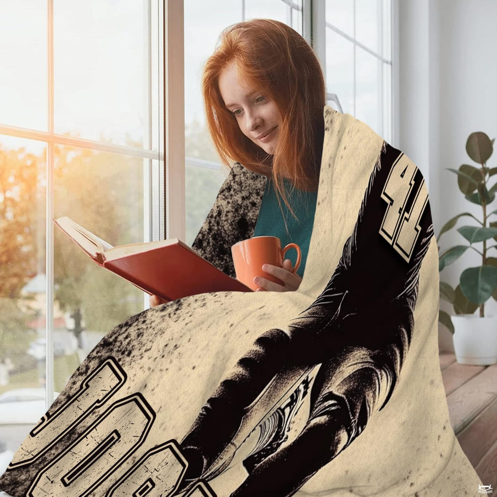 Person wrapped comfortably in sports throw blanket while reading a book beside a sunny window.