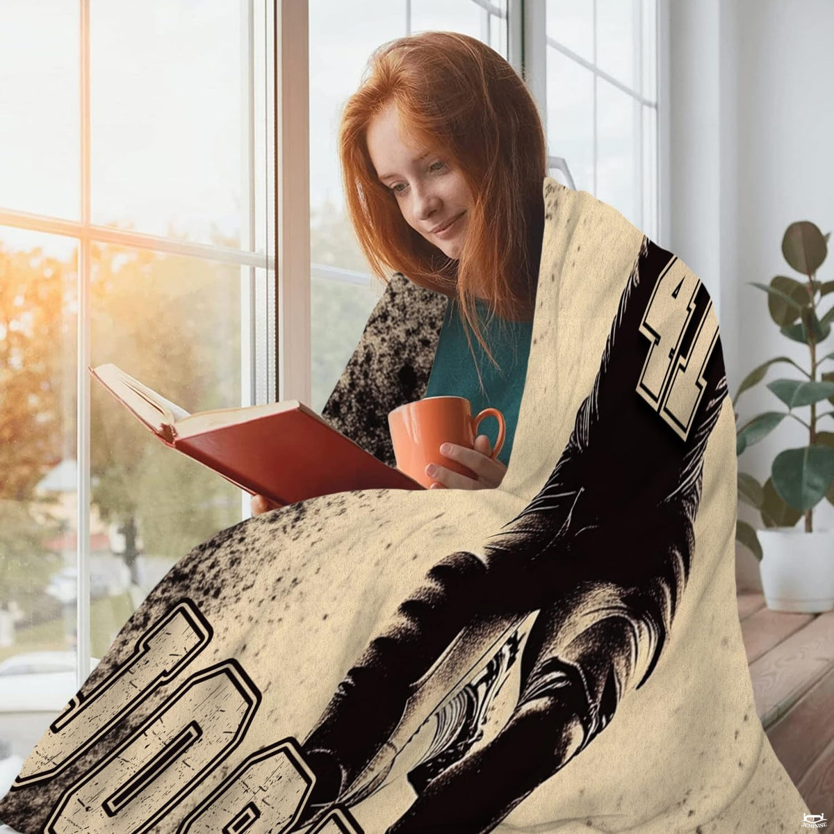 Person wrapped comfortably in sports throw blanket while reading a book beside a sunny window.