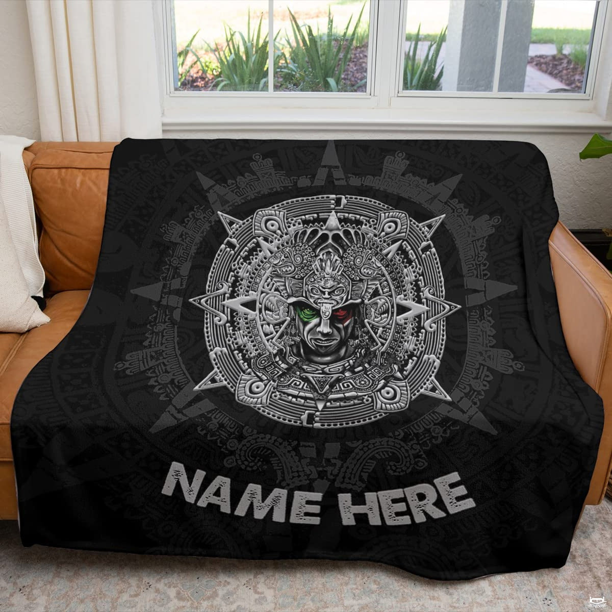 Aztec sun stone calendar textile displayed across a brown couch in sunlit living room.