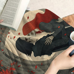 Close-up detail of embracing skeletal lovers and crimson leaf artwork on throw blanket