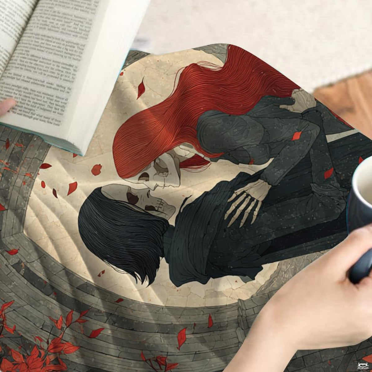 Close-up detail of embracing skeletal lovers and crimson leaf artwork on throw blanket