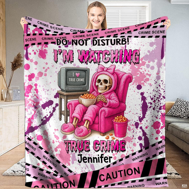 Woman holding up full size pink true crime blanket displaying skeleton in armchair eating popcorn