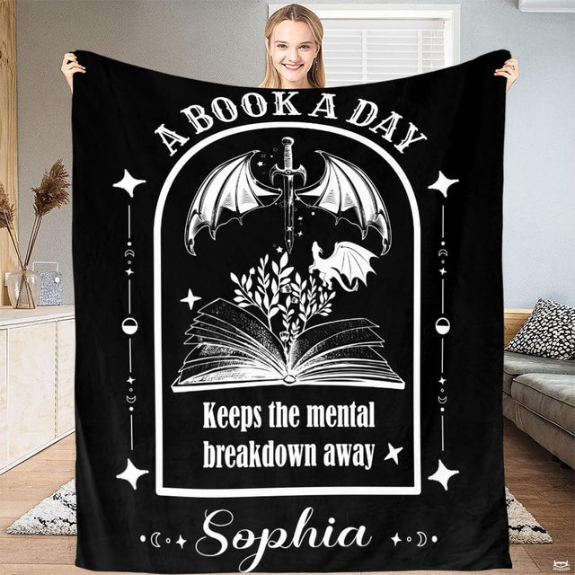 Full view of black throw blanket with white gothic arched graphic of winged dagger, dragon, and botanical foliage.