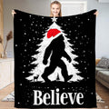 Christmas Bigfoot throw blanket featuring Sasquatch in Santa hat walking past snowy holiday tree with star