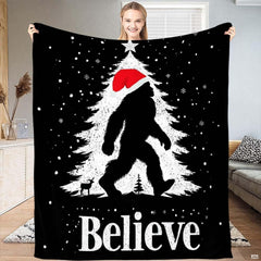 Christmas Bigfoot throw blanket featuring Sasquatch in Santa hat walking past snowy holiday tree with star