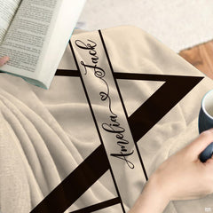 Close-up detail of split initial letter and laurel branch artwork on throw blanket