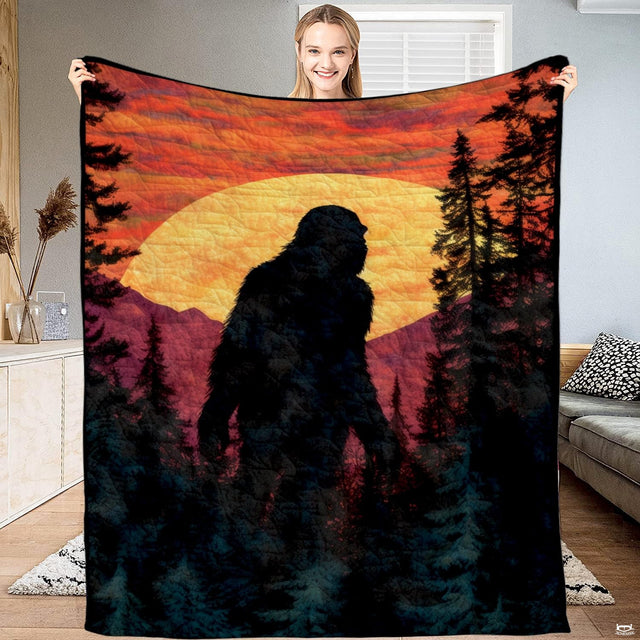 Bigfoot mountain sunset blanket featuring Sasquatch silhouette and glowing sun in pine forest.