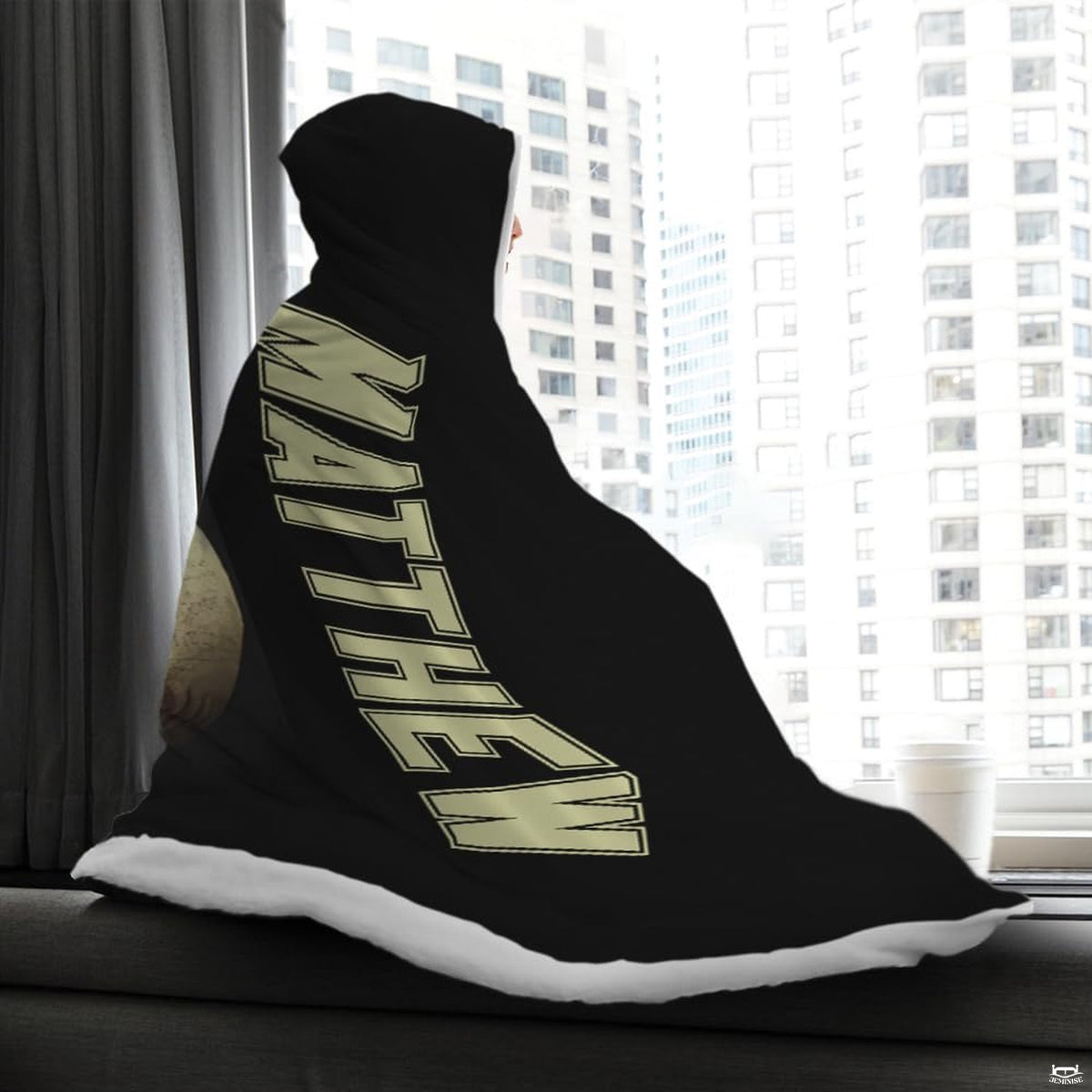 Person wrapped in the sports graphic textile sitting on a window bench looking out at city buildings.