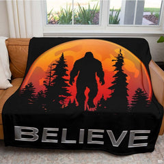 Bigfoot forest graphic throw blanket draped across brown leather living room couch near window.