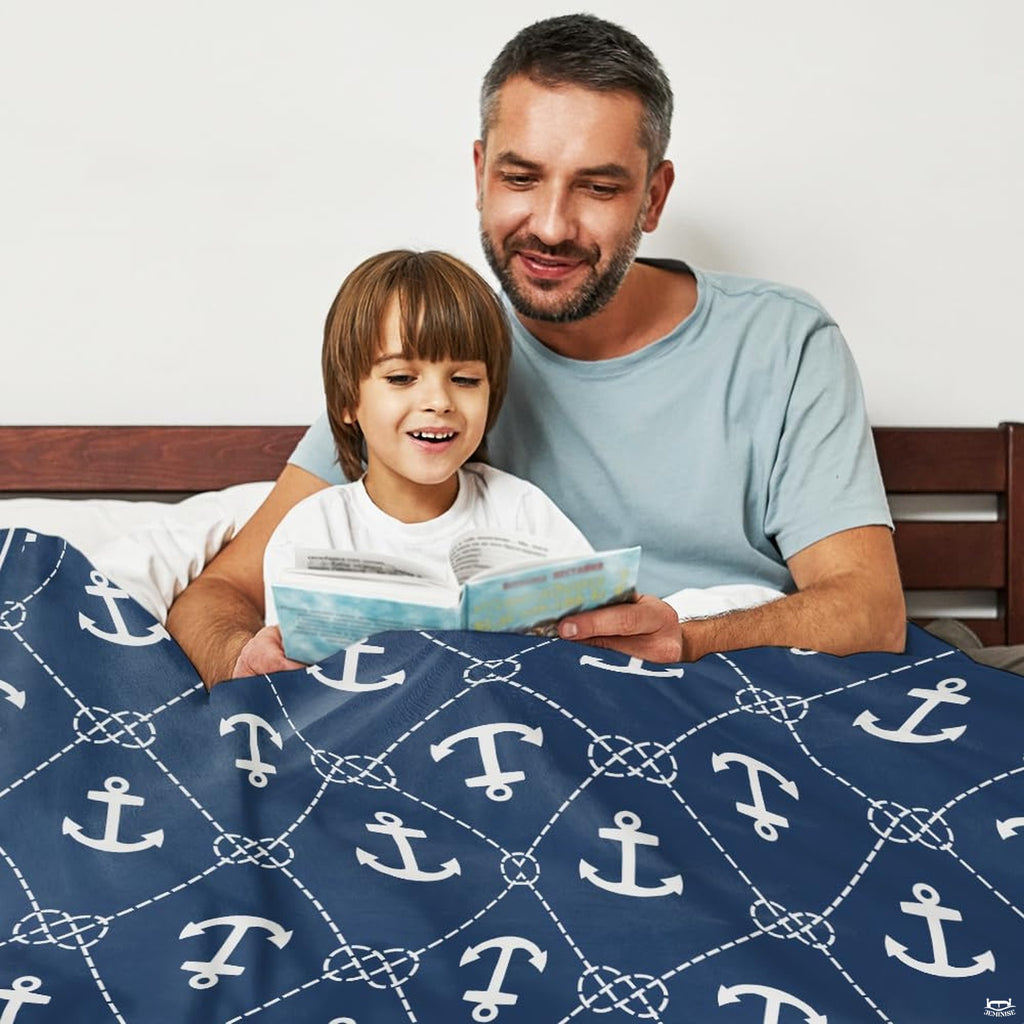 Father and son reading storybook together in bed covered with navy nautical anchor graphic blanket.