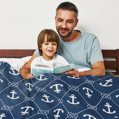 Father and son reading storybook together in bed covered with navy nautical anchor graphic blanket.
