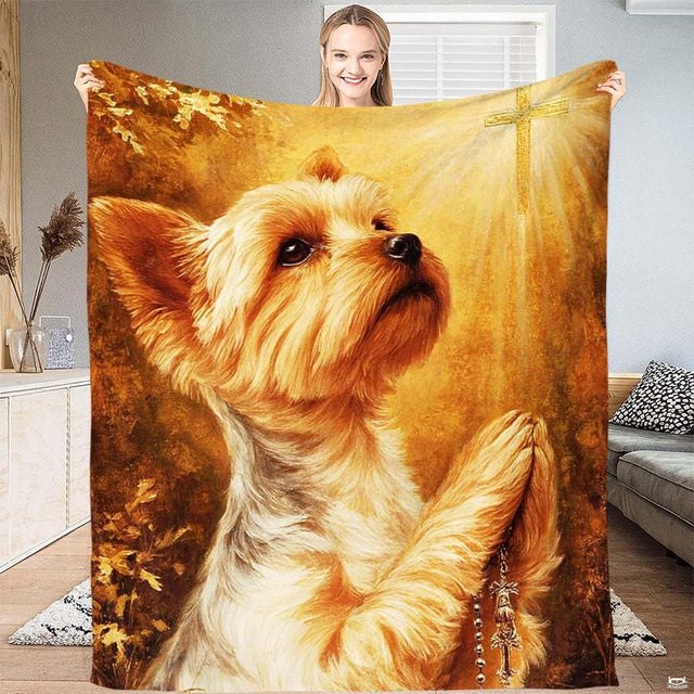 Praying Yorkshire Terrier dog holding a rosary beneath a glowing golden cross throw blanket