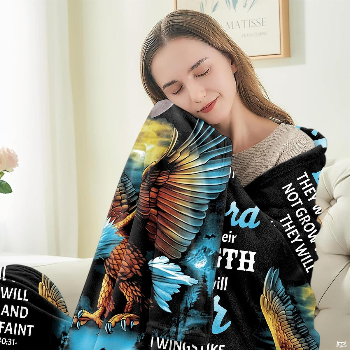 Person seated indoors wrapped in a flying raptor and golden cross devotional blanket.