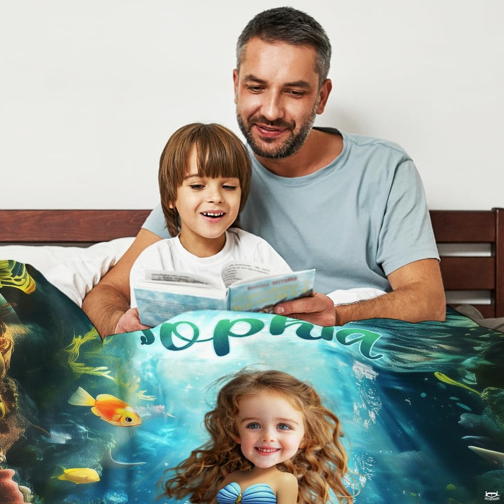 Father and son reading storybook together in bed covered with colorful mermaid graphic throw blanket.