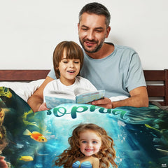 Father and son reading storybook together in bed covered with colorful mermaid graphic throw blanket.