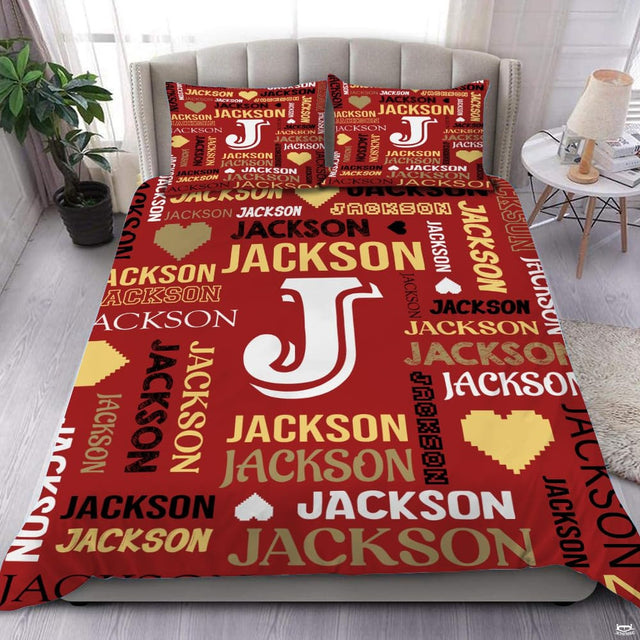 Close-up view of bedding detailing bold initial outline, pixel heart motifs, and golden typography accents