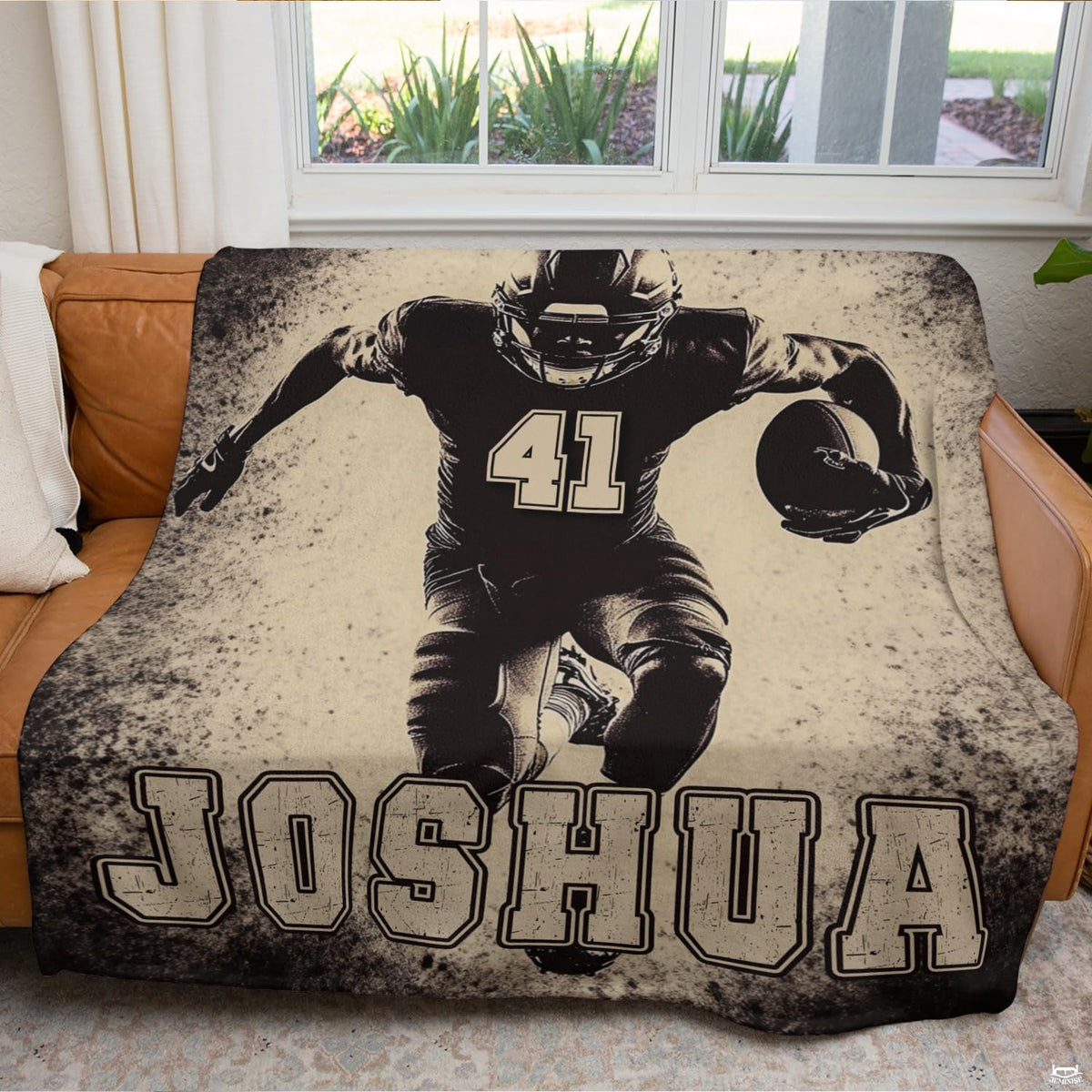 Sports graphic throw blanket draped neatly over a brown leather couch in a modern living space.