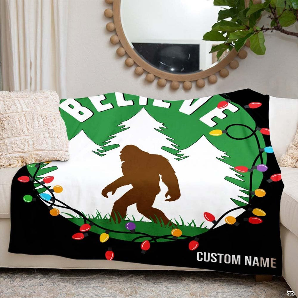 Brown Bigfoot walking in snowy forest framed by Christmas lights wreath and arched lettering, view 4.