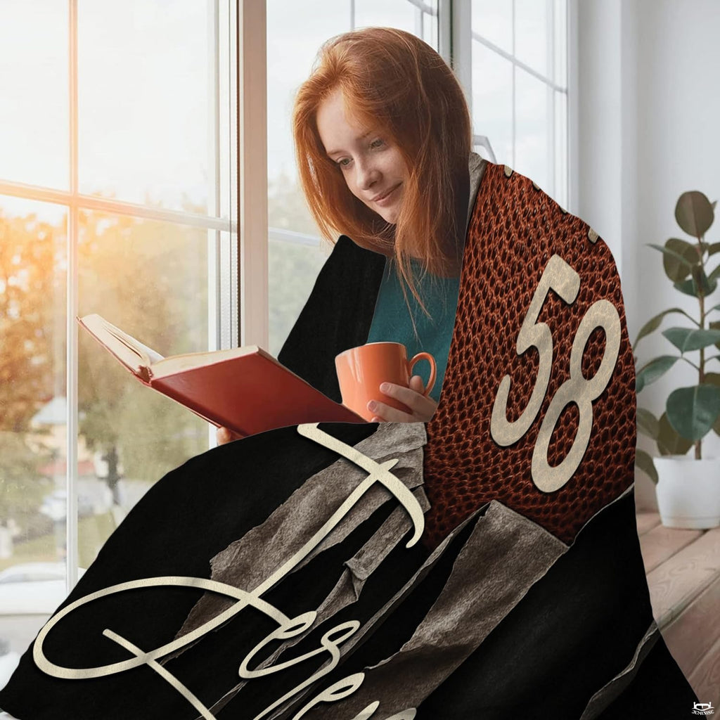 Woman wrapped comfortably in football heart throw blanket while enjoying a warm beverage by the window.